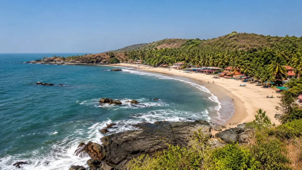 Gokarna beach with blue waters, rocky cliffs, sandy shoreline and lush green palm trees along the Karnataka coast.