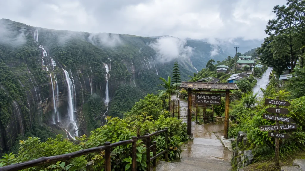 Mawlynnong village in Meghalaya surrounded by lush hills, waterfalls, misty clouds and a scenic monsoon landscape.
